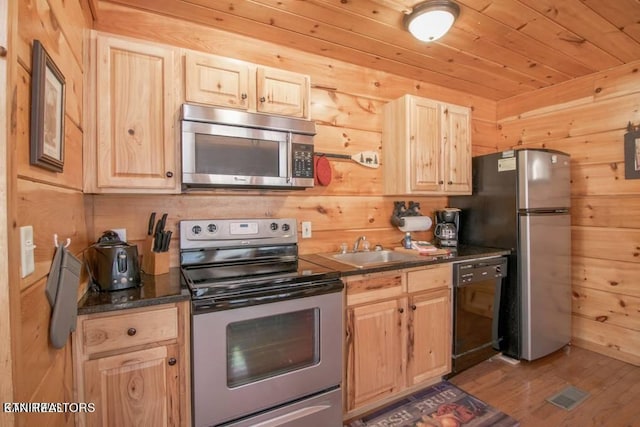 kitchen with light hardwood / wood-style floors, wood walls, stainless steel appliances, light brown cabinetry, and sink