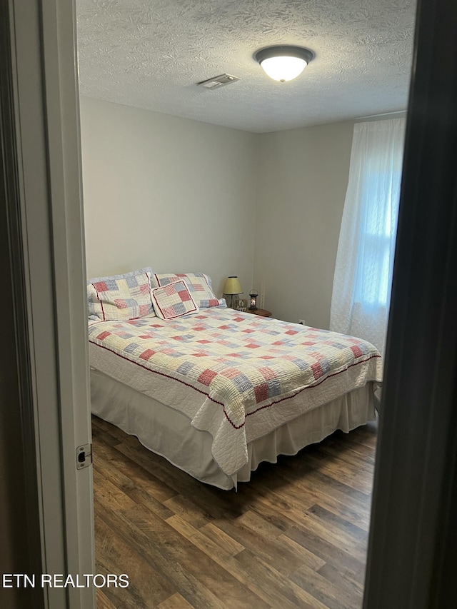 bedroom with visible vents, dark wood-style flooring, and a textured ceiling