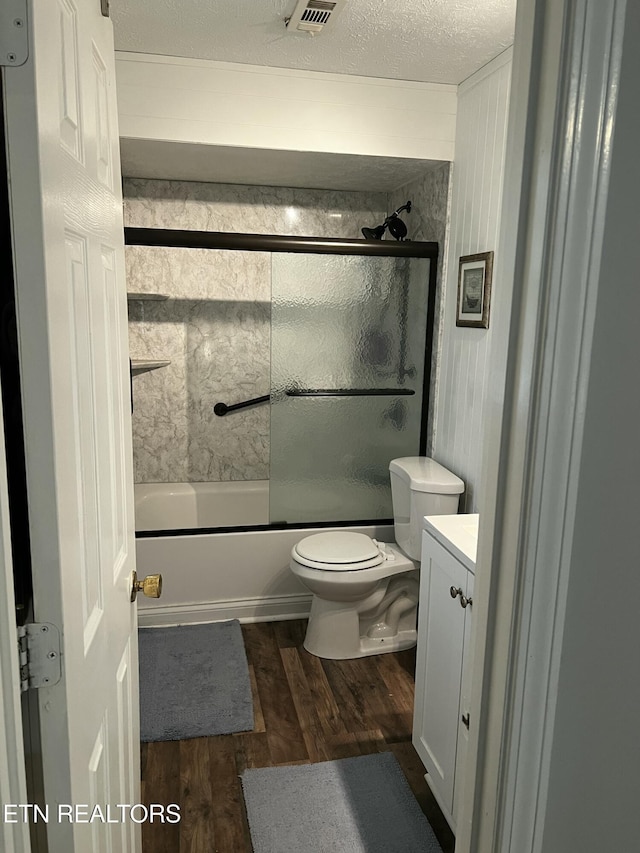 bathroom with toilet, a textured ceiling, wood finished floors, shower / bath combination with glass door, and vanity