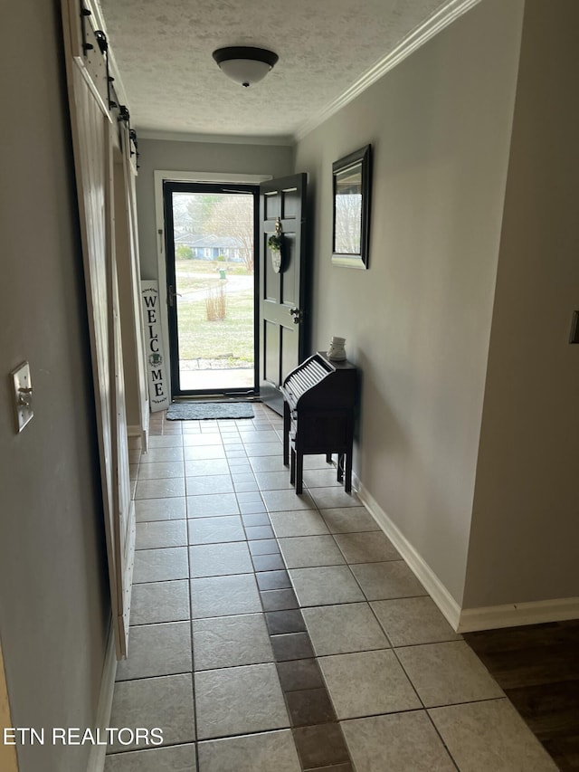 hall featuring tile patterned flooring, baseboards, a barn door, ornamental molding, and a textured ceiling