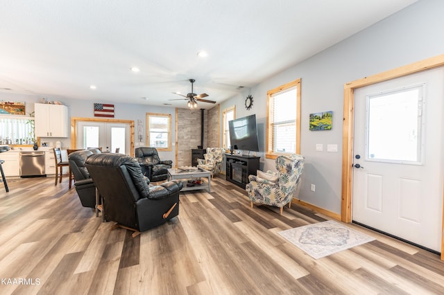 living room with french doors, light hardwood / wood-style floors, ceiling fan, and a wood stove