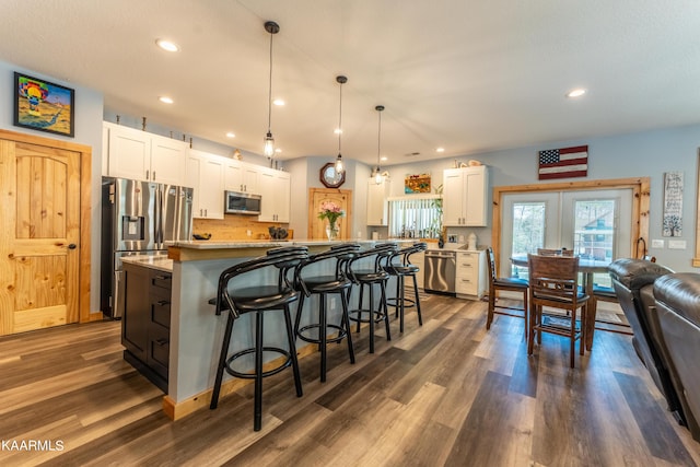 kitchen with dark hardwood / wood-style flooring, decorative light fixtures, appliances with stainless steel finishes, white cabinetry, and a breakfast bar area