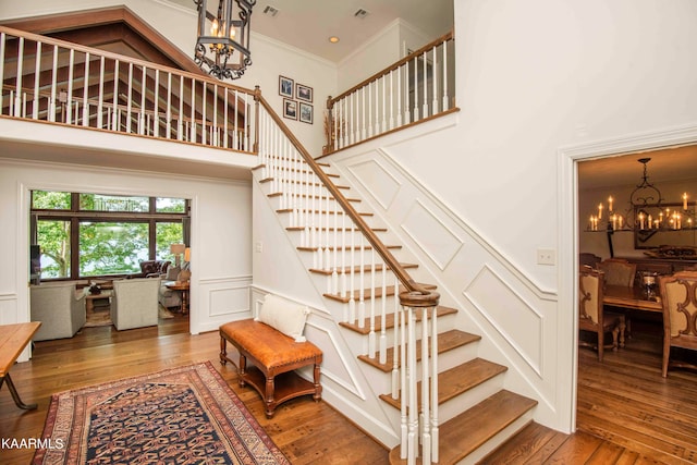 stairway featuring a high ceiling, an inviting chandelier, ornamental molding, and hardwood / wood-style flooring