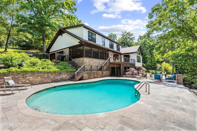 view of swimming pool with a patio area, a wooden deck, and a sunroom