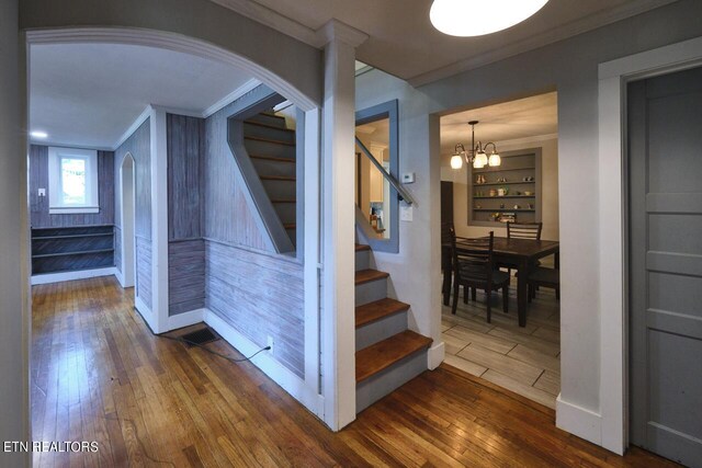 stairway with ornamental molding, a notable chandelier, and wood-type flooring