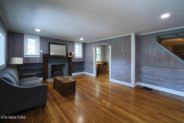 living room with crown molding, hardwood / wood-style flooring, a brick fireplace, and wood walls