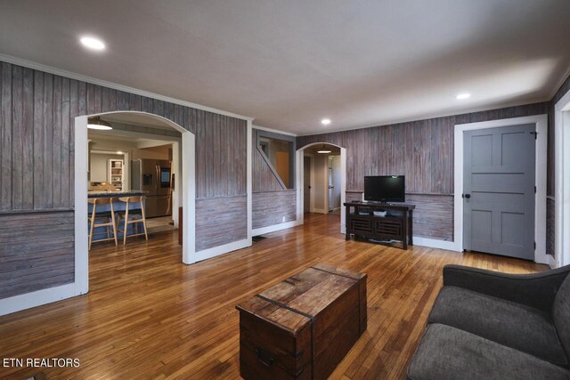 living room with crown molding, wooden walls, and hardwood / wood-style flooring