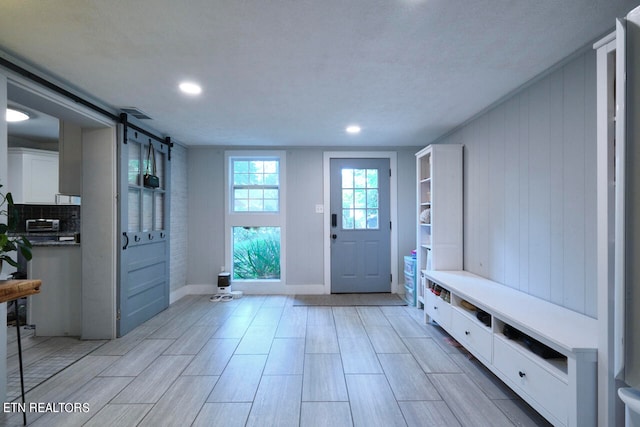 mudroom with a textured ceiling, light hardwood / wood-style flooring, and a barn door