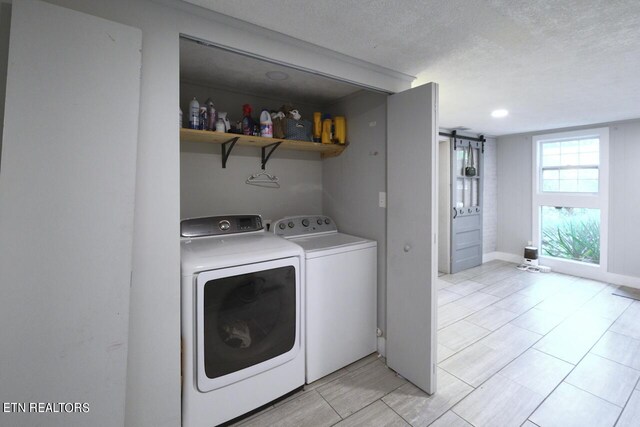 laundry area with a barn door, washing machine and clothes dryer, light tile patterned flooring, and a textured ceiling