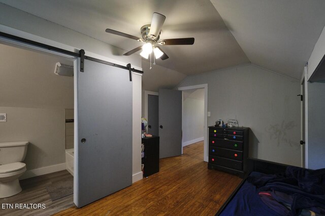 bedroom with hardwood / wood-style flooring, vaulted ceiling, a barn door, ceiling fan, and connected bathroom