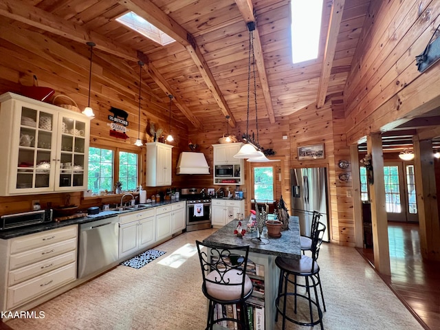 kitchen featuring hanging light fixtures, wooden ceiling, beam ceiling, wood walls, and appliances with stainless steel finishes