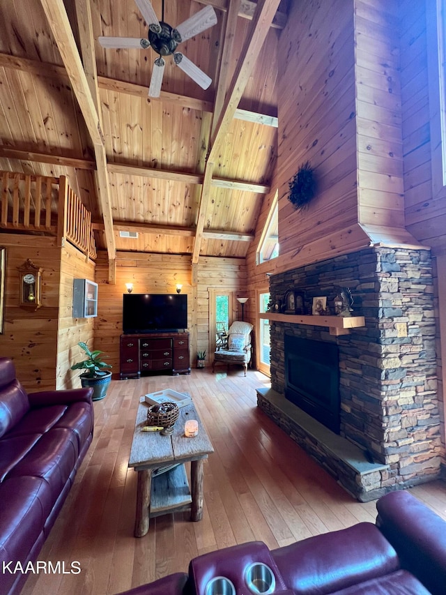 living room with hardwood / wood-style flooring, ceiling fan, wooden ceiling, wooden walls, and a stone fireplace