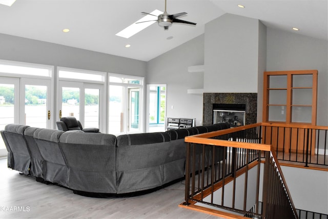 living room featuring a skylight, high vaulted ceiling, ceiling fan, and light wood-type flooring