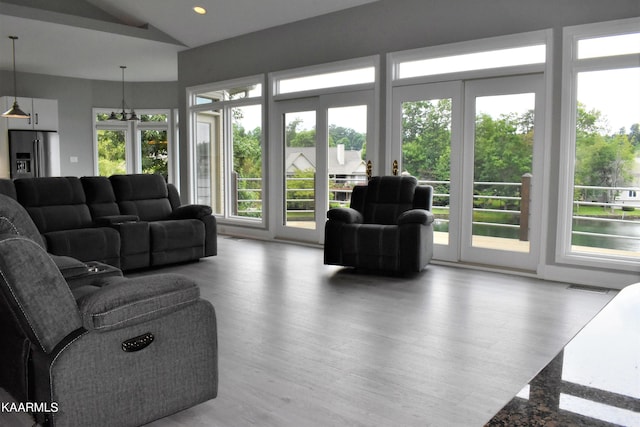 living room with a notable chandelier, plenty of natural light, light hardwood / wood-style floors, and vaulted ceiling