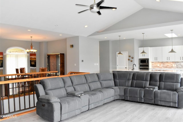 living room featuring sink, light wood-type flooring, high vaulted ceiling, and ceiling fan with notable chandelier