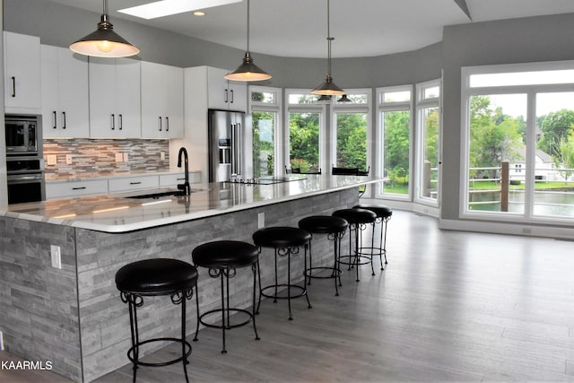 kitchen with appliances with stainless steel finishes, white cabinets, light hardwood / wood-style flooring, pendant lighting, and sink