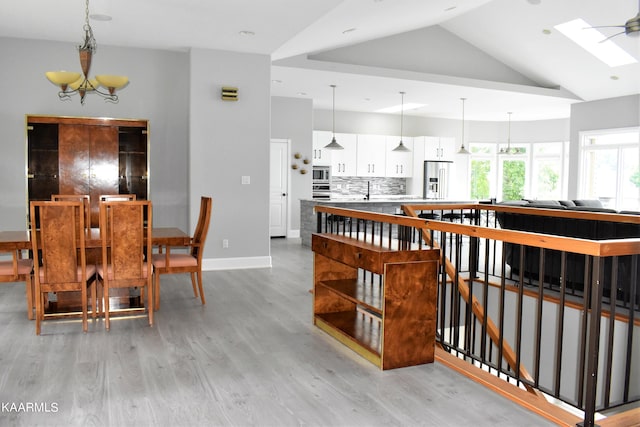 interior space with a skylight, a notable chandelier, light hardwood / wood-style flooring, and high vaulted ceiling