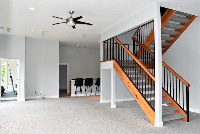 stairway with ceiling fan, light carpet, and a high ceiling