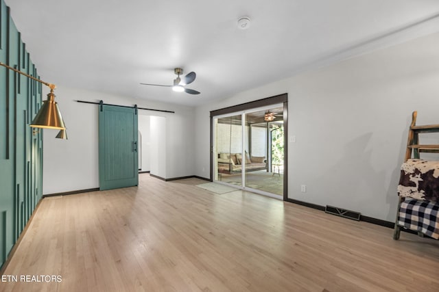 spare room featuring ceiling fan, a barn door, and light hardwood / wood-style floors