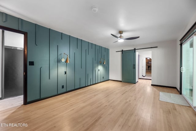 spare room with a barn door, ceiling fan, and light hardwood / wood-style floors