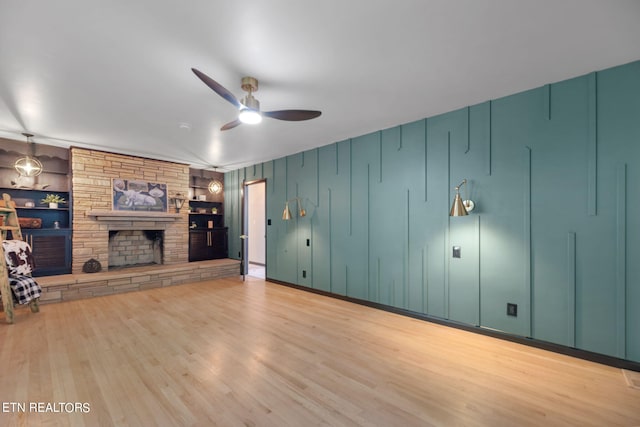 unfurnished living room with light wood-type flooring, built in features, ceiling fan, and a stone fireplace