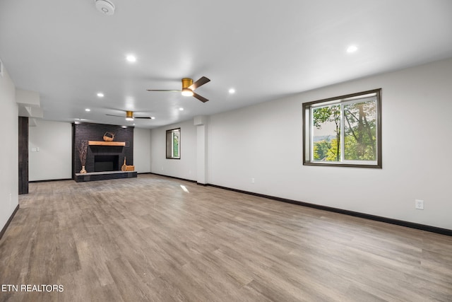 unfurnished living room featuring light wood-type flooring, ceiling fan, brick wall, and a brick fireplace