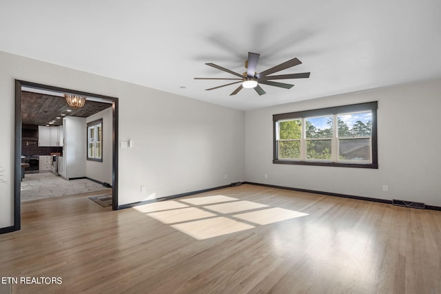 unfurnished room with ceiling fan with notable chandelier and light hardwood / wood-style floors