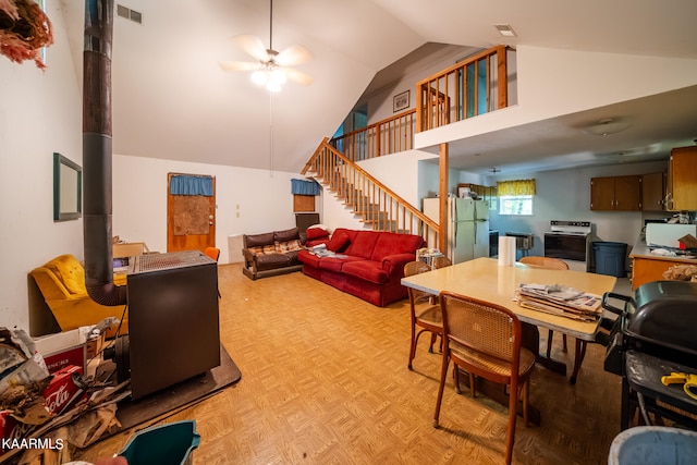 living room with ceiling fan, light parquet flooring, high vaulted ceiling, and a wood stove