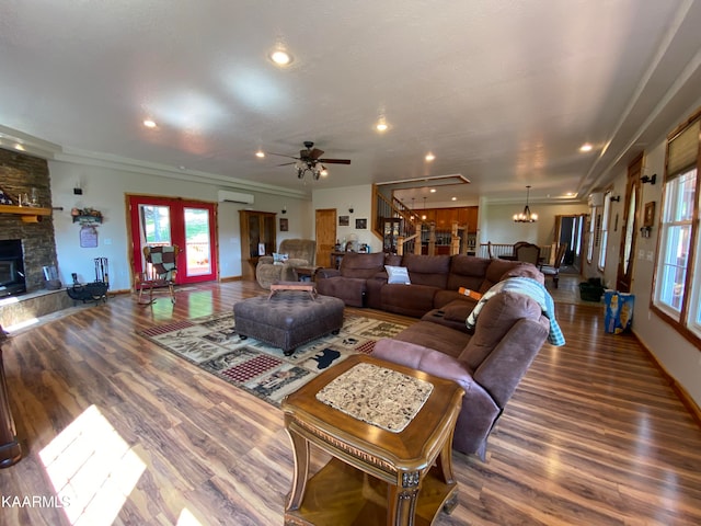 living room featuring a stone fireplace, hardwood / wood-style flooring, ceiling fan with notable chandelier, and a wall unit AC