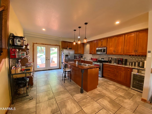 kitchen with beverage cooler, appliances with stainless steel finishes, french doors, an island with sink, and a breakfast bar area