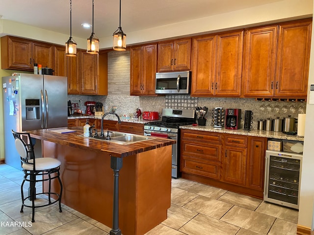 kitchen featuring stainless steel appliances, a kitchen island with sink, beverage cooler, hanging light fixtures, and sink