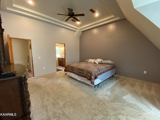 bedroom featuring ceiling fan, connected bathroom, a tray ceiling, and carpet flooring