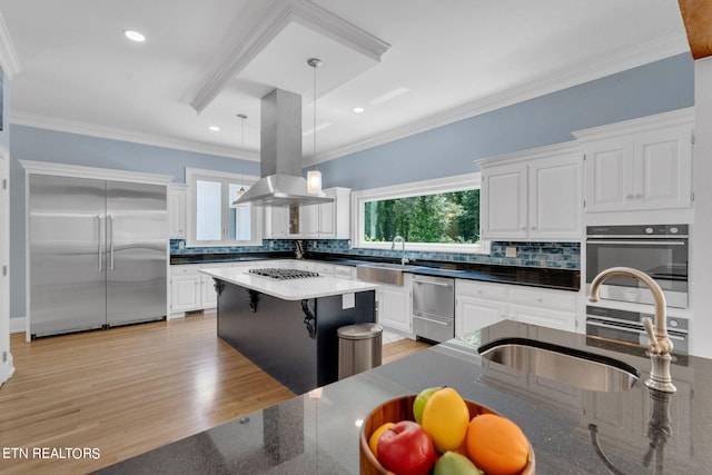 kitchen featuring island range hood, white cabinetry, hanging light fixtures, and appliances with stainless steel finishes