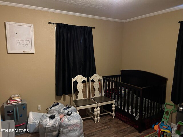 bedroom featuring a crib, crown molding, and dark wood-type flooring