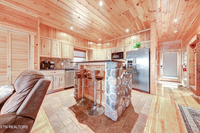 kitchen with appliances with stainless steel finishes, a kitchen island, wood ceiling, wooden walls, and a kitchen breakfast bar