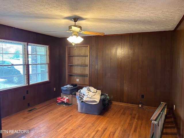 living area featuring ceiling fan, a textured ceiling, wood walls, and dark wood-type flooring