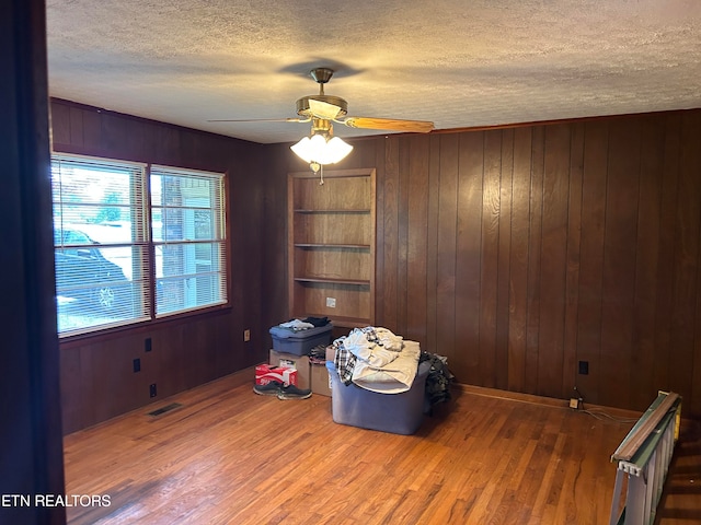 miscellaneous room with wood walls, a textured ceiling, ceiling fan, and hardwood / wood-style flooring