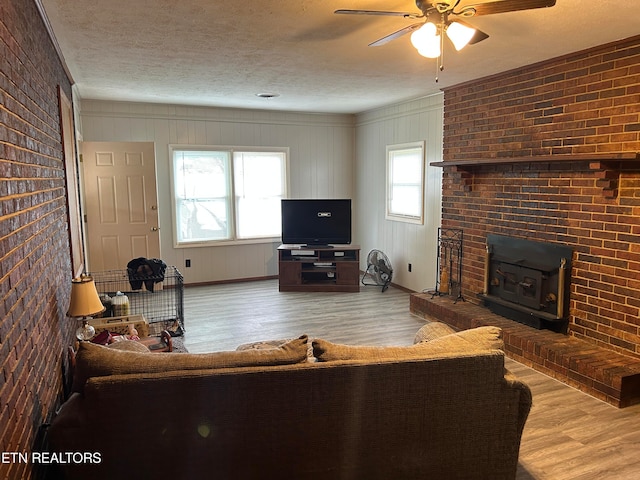 living room featuring brick wall, a wood stove, ceiling fan, and hardwood / wood-style flooring