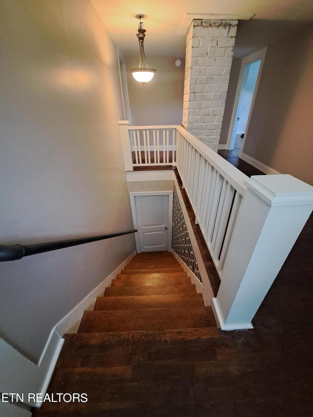 stairway with dark hardwood / wood-style floors and brick wall