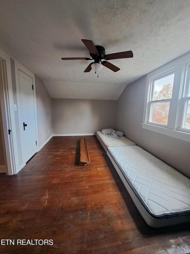 unfurnished bedroom with ceiling fan, dark hardwood / wood-style flooring, lofted ceiling, and a textured ceiling