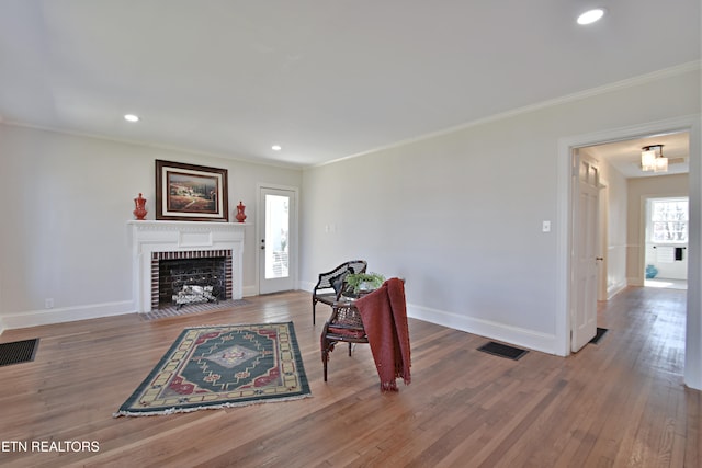 living area featuring a brick fireplace, visible vents, and wood finished floors