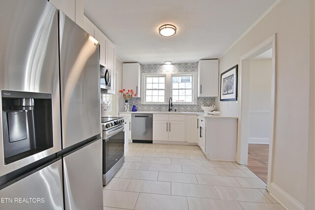 kitchen featuring stainless steel appliances, a sink, white cabinets, light countertops, and backsplash