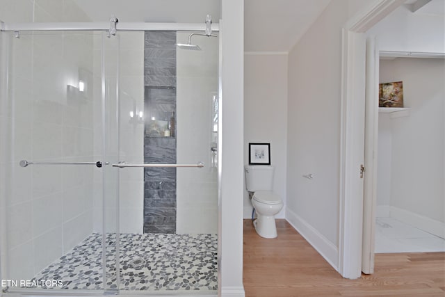 bathroom featuring toilet, a shower stall, baseboards, and wood finished floors