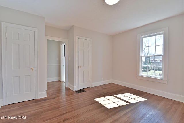 unfurnished bedroom featuring visible vents, baseboards, and wood finished floors