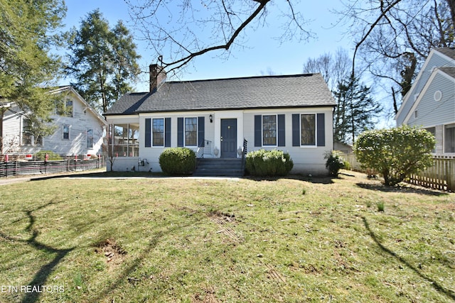 view of front of home with roof with shingles, a front lawn, a chimney, and fence