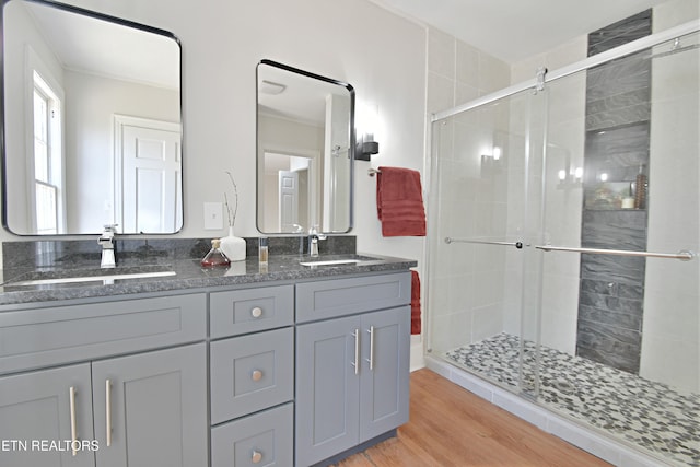 full bath featuring double vanity, a stall shower, a sink, and wood finished floors