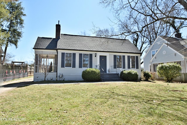 view of front of home with roof with shingles, a chimney, fence, and a front yard