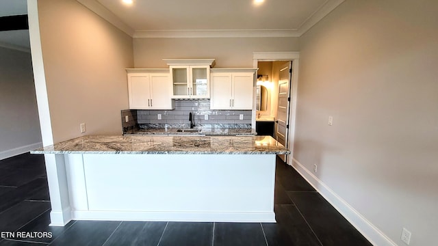 kitchen featuring tasteful backsplash, white cabinets, a peninsula, light stone countertops, and a sink