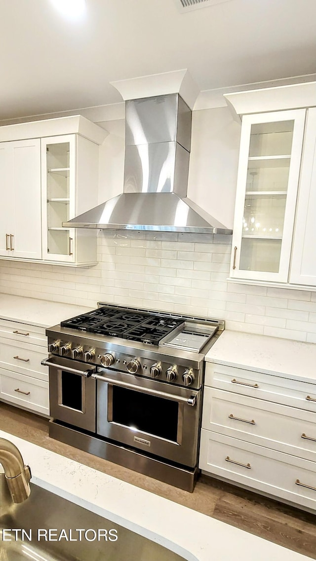 kitchen with wall chimney exhaust hood, tasteful backsplash, white cabinets, and double oven range