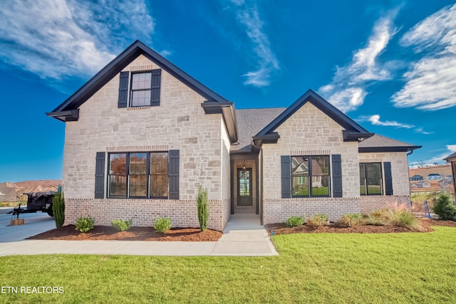 french country style house featuring a shingled roof, stone siding, brick siding, and a front lawn